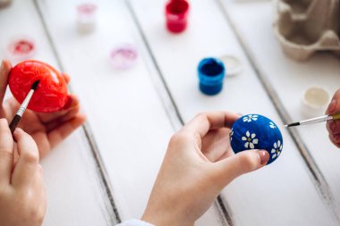 Kadın elleri mavi Paskalya yumurtalarını beyaz arka planda tutuyor. Yumurta boyama geleneği