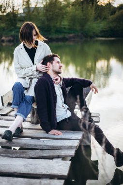 Genç hippi aşığı çift nehir kıyısında iskelede dinleniyor. Erkek ve kadın gün batımında eğleniyor ve dinleniyorlar.. 