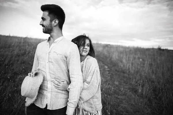 恋爱中的幸福夫妻在田野的天空中拥抱 亲吻和微笑 女孩手里拿着帽子 — 图库照片