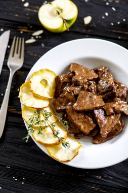 Beyaz tabakta elmalı domuz ciğeri. Dümdüz uzanıyordu karanlığa