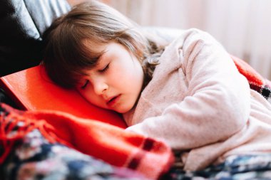 Karantina sırasında kanepede kitap okuyan bir kız. Coronavirus 'un yayılmasını engellemek için evde kal.