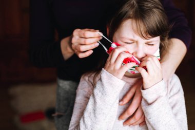 Anne, kızına onu virüsten korumak için parlak karpuz izli bir maske takıyor. Koronavirüs salgını. Corona 'nın yayılmasını engellemek için evde kal..