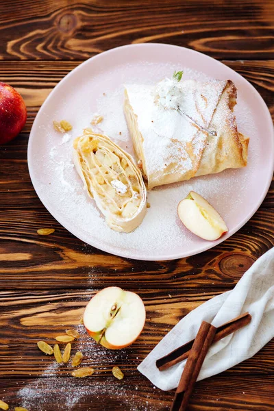 Healthy Home made sweet Apple strudel with raisins and cinnamon on wooden background with blooming fruit branches. Flat Lay. Quarantine kitchen