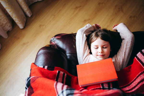 Girl reading a book lying on the couch during quarantine. Stay home to stop the spread of Coronavirus