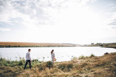 Sahilde yürüyen, kucaklaşan, arka planda gülümseyen güzel bir çift. Erkek ve kız hipster seyahati.