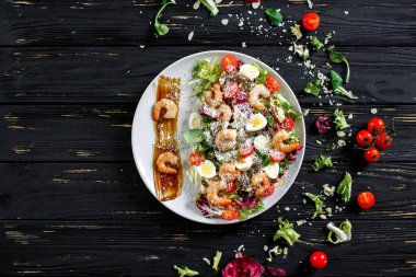 Karanlık bir arka planda karides salatası. Karides, marul, bıldırcın yumurtası, vişneli domates, parmesan, baharatlı sos.