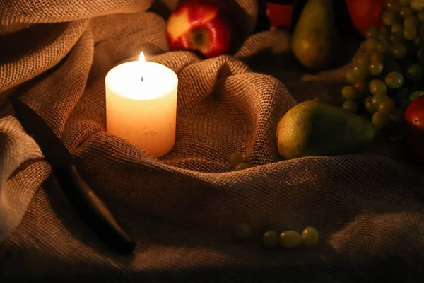 Fehér gyertya lágy fény fekete késsel és gyümölcsökkel: alma, körte és szőlő zsákvászon asztalterítő ősz csendélet — Stock Fotó