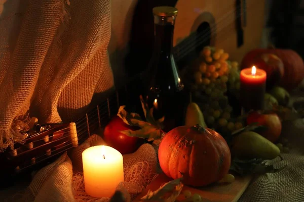 Життєвий врожай гарбуза, груш, яблук, винограду та свічок м'яке світло з пляшкою вина та гітарою на вереску — стокове фото
