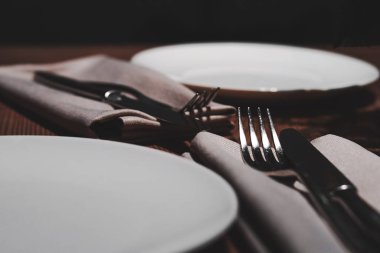 Restoran masası servisi. Beyaz tabaklar, bez peçeteler, çatallar ve ahşap masa üzerinde bıçaklar..