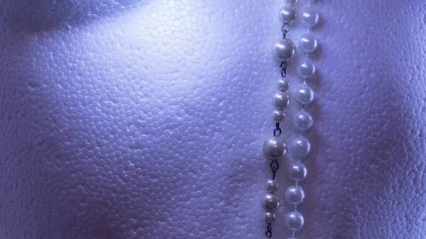 Fondo blanco texturizado de espuma de poliestireno con tonos claros azules y 2 tiras de collares de perlas . — Foto de Stock