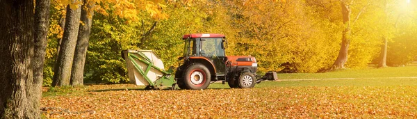 Barredora de vacío remolcada por un trabajo de tractor en el parque de otoño. — Foto de Stock