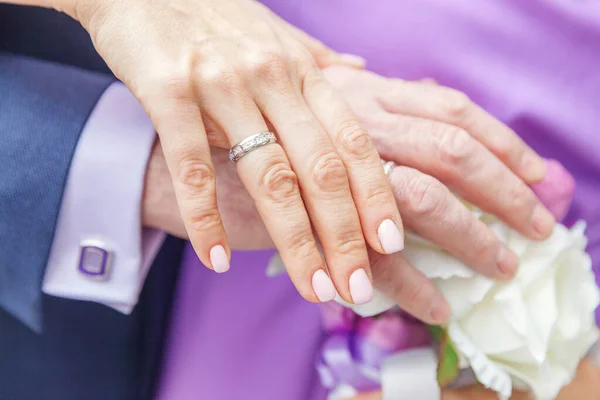 Bruden och brudgummen händer med vigselringar mot bakgrund av brudbukett blommor — Stockfoto