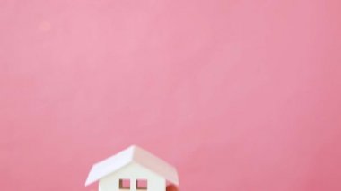 Pembe arka planda izole edilmiş minyatür oyuncak evi tutan kadın.