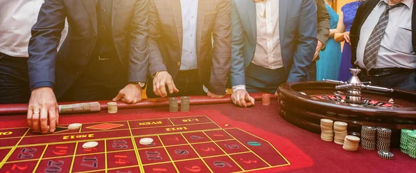 Grupo de pessoas atrás da roleta mesa de jogo em banner casino de luxo — Fotografia de Stock