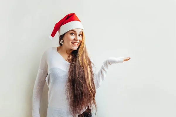 Belle fille en chapeau rouge du Père Noël montrant la main ouverte de la paume réconfortée sur fond blanc — Photo