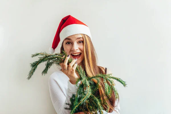 Belle fille en chapeau rouge Père Noël tenant branche de sapin isolé sur fond blanc regardant heureux et excité. Une jeune femme dépeint de vraies émotions. Joyeux Noël et Nouvel An — Photo