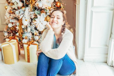 Noel arifesinde Noel ağacının yanında hediye kutusu olan genç bir kız. Kış dekorasyonuyla aydınlık odada genç bir kadın. Noel Yeni Yıl Kutlama Konsepti Zamanı