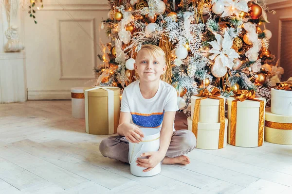Маленький мальчик с подарочной коробкой возле елки в канун Рождества дома. Молодой парень в светлой комнате с зимним декором. Счастливая семья дома. Рождество Новый год декабрь время для празднования концепции — стоковое фото