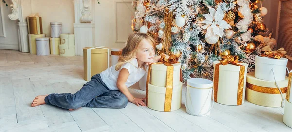 Bambina con scatola regalo vicino all'albero di Natale la vigilia di Natale a casa. Ragazzo giovane in camera leggera con decorazione invernale. Famiglia felice a casa. Capodanno dicembre tempo per il concetto di celebrazione Banner — Foto Stock