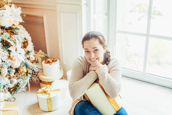 Junges Mädchen mit Geschenkbox in der Nähe des Weihnachtsbaums an Heiligabend zu Hause. junge Frau in hellem Raum mit Winterdekoration. Weihnachten Neujahr Dezember Zeit für Feier-Konzept — Stockfoto