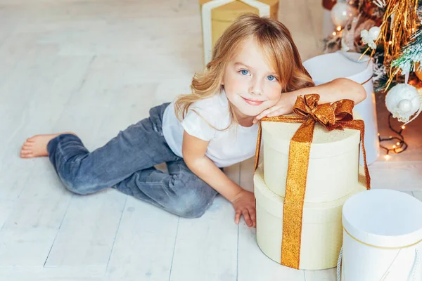 Маленькая девочка с подарочной коробкой возле елки в канун Рождества дома. Молодой парень в светлой комнате с зимним декором. Счастливая семья дома. Рождество Новый год декабрь время для празднования концепции — стоковое фото
