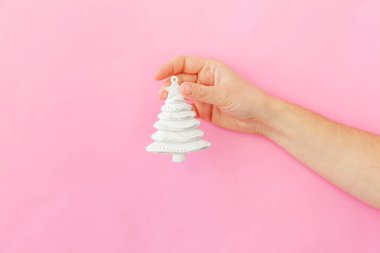 Simply minimal design female woman hand holding Christmas ornament fir tree isolated on pink pastel colorful trendy background clipart