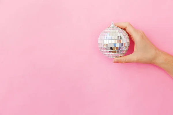 Просто минимальный дизайн женская рука держа Рождественский орнамент диско мяч изолирован на розовый пастель красочный модный фон — стоковое фото