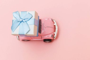 Simply design pink vintage retro toy car delivering gift box on roof isolated on trendy pastel pink background. Christmas New Year birthday Valentine's day celebration present romantic concept