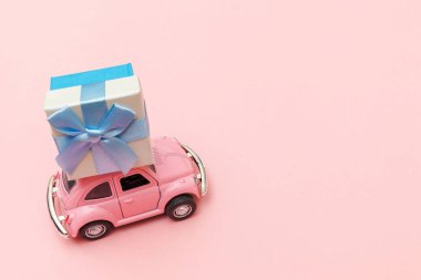 Simply design pink vintage retro toy car delivering gift box on roof isolated on trendy pastel pink background. Christmas New Year birthday Valentine's day celebration present romantic concept