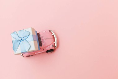 Simply design pink vintage retro toy car delivering gift box on roof isolated on trendy pastel pink background. Christmas New Year birthday Valentine's day celebration present romantic concept