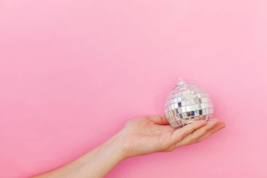 En az tasarım kadın, elinde Noel süsü olan bir disko topu pembe renkli arka planda izole edilmiş.