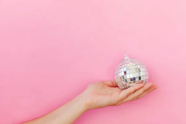 Просто минимальный дизайн женская рука держа Рождественский орнамент диско мяч изолирован на розовый пастель красочный модный фон — стоковое фото