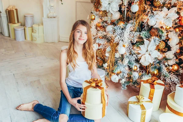 Teenagermädchen mit Geschenkbox am Weihnachtsbaum an Heiligabend zu Hause. Junge Frau in hellem Raum mit Winterdekoration. Weihnachten Silvester Dezemberzeit für Festkonzept — Stockfoto