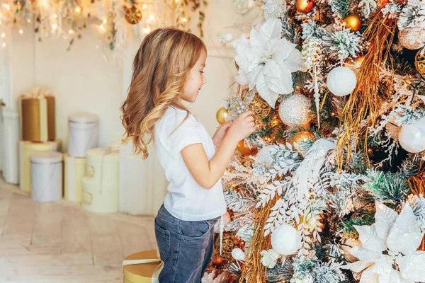 Dívka zdobí vánoční stromeček na Štědrý večer doma. Mladý kluk v osvětlené místnosti se zimní výzdobou. Šťastná rodina doma. Vánoce Nový rok prosinec čas na oslavu konceptu — Stock fotografie