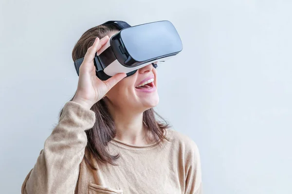 身穿虚拟现实VR眼镜头盔头戴白色背景头盔的年轻女性微笑。智能手机与虚拟现实护目镜一起使用。技术、模拟、高科技、电子游戏概念. — 图库照片