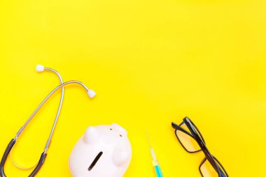 Tıp doktor ekipman stetoskop veya fonndoskop kumbara gözlük şırınga trendy sarı arka plan üzerinde izole. Sağlık mali check-up veya sağlık sigortası maliyetleri kavramı için tasarruf