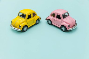 Mavi pastel renkli arka planda izole edilmiş iki adet sarı, eski model oyuncak arabaya sahip basit bir tasarım. Otomobil ve ulaşım sembolü. Şehir trafiği konsepti. Metin için alanı kopyala