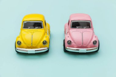 Mavi pastel renkli arka planda izole edilmiş iki adet sarı, eski model oyuncak arabaya sahip basit bir tasarım. Otomobil ve ulaşım sembolü. Şehir trafiği konsepti. Metin için alanı kopyala