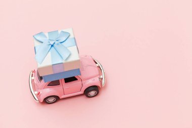 Simply design pink vintage retro toy car delivering gift box on roof isolated on trendy pastel pink background. Christmas New Year birthday Valentine's day celebration present romantic concept.