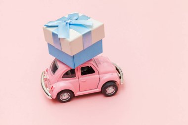 Pembe eski model oyuncak araba tasarımı. Moda pastel pembe arka planda izole edilmiş çatıda hediye kutusu dağıtımı. Noel, yeni yıl doğum günü Sevgililer Günü, hediye romantik konsept