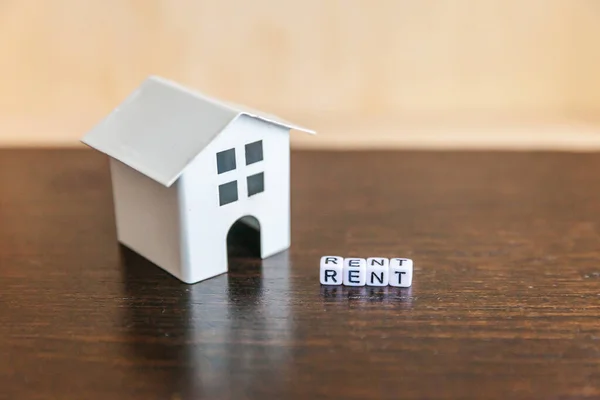 Casa modelo de juguete miniatura con inscripción RENT letters palabra sobre fondo de madera. Eco Village, fondo ambiental abstracto. Bienes raíces hipoteca propiedad seguro dulce hogar ecología alquiler concepto — Foto de Stock