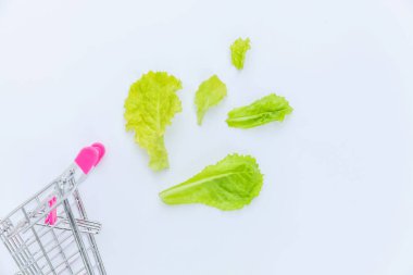 Small supermarket grocery push cart for shopping with green lettuce leaves isolated on white background clipart