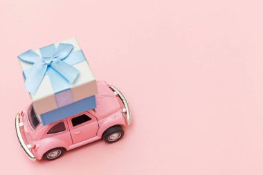 Simply design pink vintage retro toy car delivering gift box on roof isolated on trendy pastel pink background. Christmas New Year birthday Valentine's day celebration present romantic concept