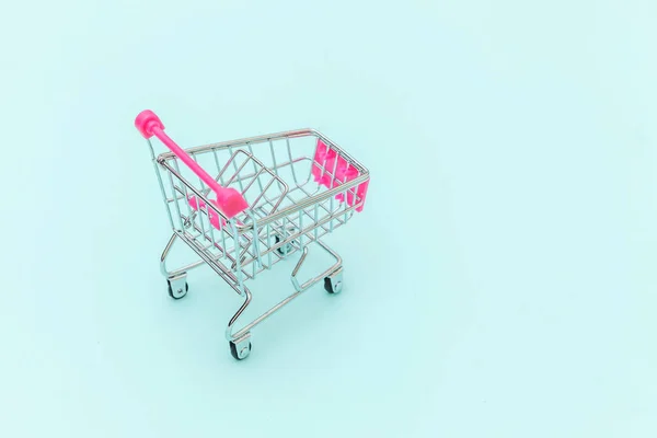 青いパステルカラーのトレンディーな背景に隔離された車輪付きのショッピングおもちゃのための小さなスーパーマーケットの食料品プッシュカートコピースペース。販売｜モールマーケットショップの消費者コンセプト. — ストック写真
