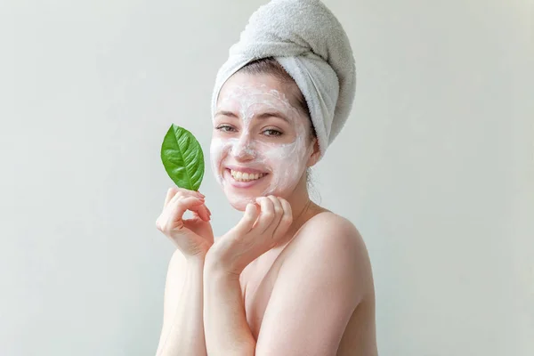 Minimal beauty woman girl in towel on head portrait applying white nourishing mask or creme on face, πράσινο φύλλο στο χέρι απομονωμένο λευκό φόντο. Καθαρισμός δέρματος eco οργανικό καλλυντικό spa έννοια. — Φωτογραφία Αρχείου