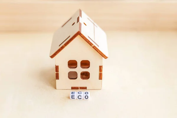 Miniature toy model house with inscription ECO letters word on wooden backdrop. Eco Village, abstract environmental background. Ecology zero waste social responsibility recycle bio home concept