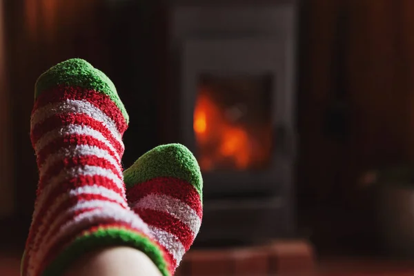 Pés pernas em roupas de inverno meias de lã na lareira em casa no inverno ou outono à noite relaxando e aquecendo — Fotografia de Stock
