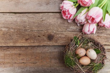 Yuvasında yosun ve pembe lale buketi olan Paskalya yumurtaları.