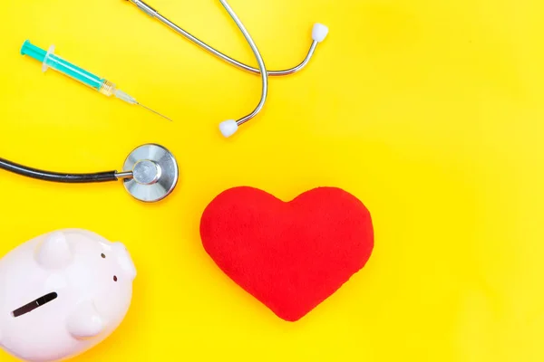 Medicine doctor equipment stethoscope or phonendoscope piggy bank red heart syringe isolated on trendy yellow background