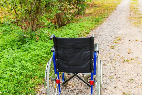 Cadeira de rodas vazia em pé na estrada no parque hospitalar à espera de atendimento ao paciente. Cadeira inválida para pessoas com deficiência estacionadas ao ar livre na natureza. Símbolo acessível para deficientes. Conceito médico de saúde . — Fotografia de Stock